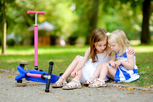 Interpersonell intelligens: större flicka hjälper liten flicka som trillat av sparkcykel