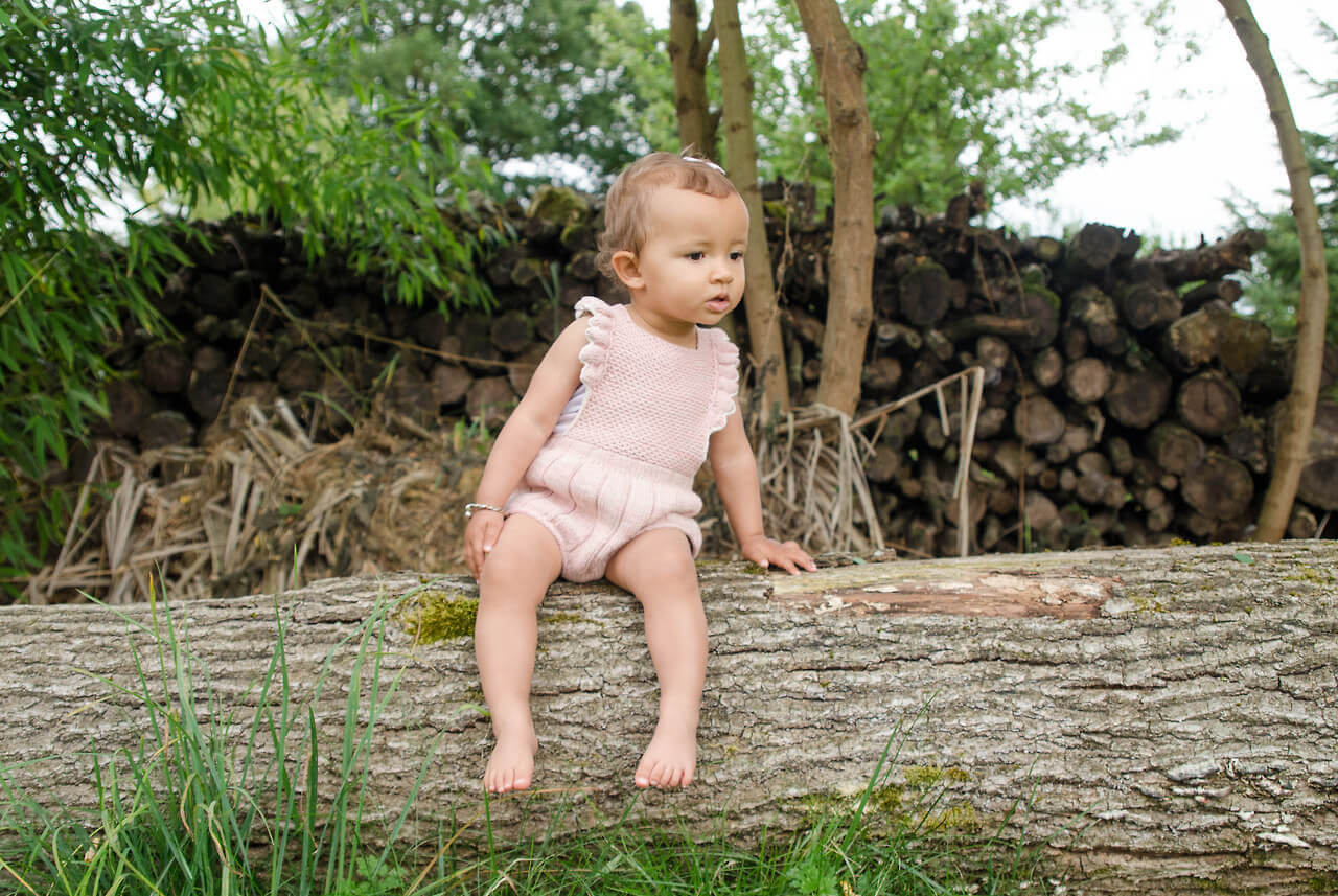 liten flicka sitter på trädstam