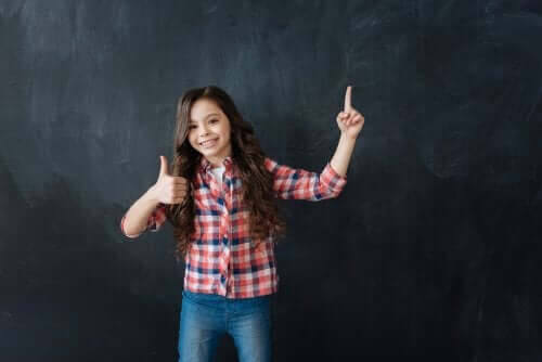 Betydelsen av att bygga motståndskraft hos barn: flicka gör tummen upp framför svart tavla