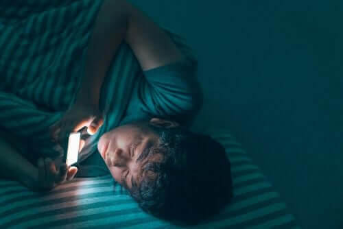Konsekvenserna av att inte sova bra under tonåren: pojke tittar på sin telefon i sängen