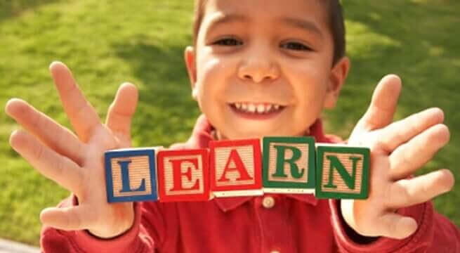 ett andra språk: pojke håller upp klossar med bokstäverna LEARN