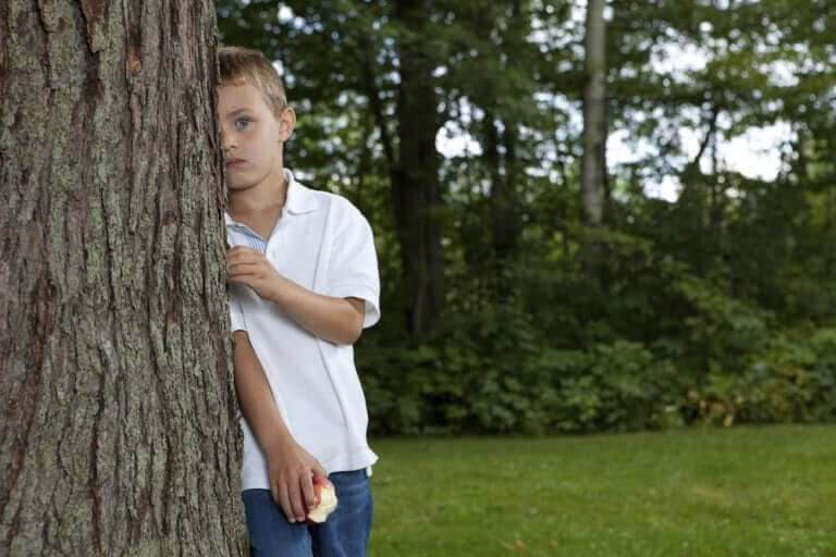 blyga och introverta barn: pojke gömmer sig halvt bakom ett träd