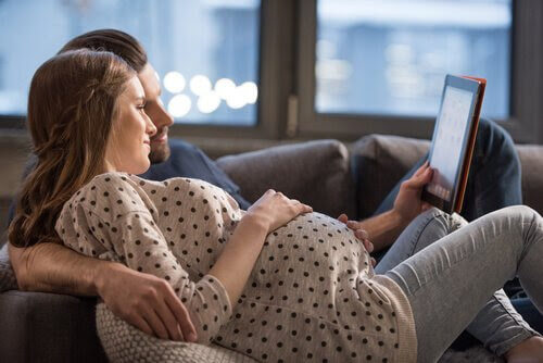 man och gravid kvinna i soffa tittar på läsplatta