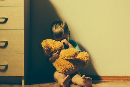 våld i familjen: pojke med nalle sitter i ett hörn