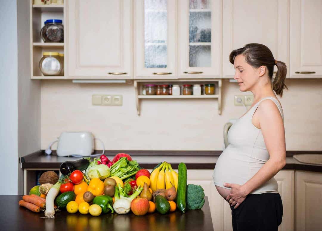 gravid kvinna i kök framför massor av grönsaker