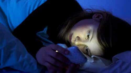 flicka med mobil i säng