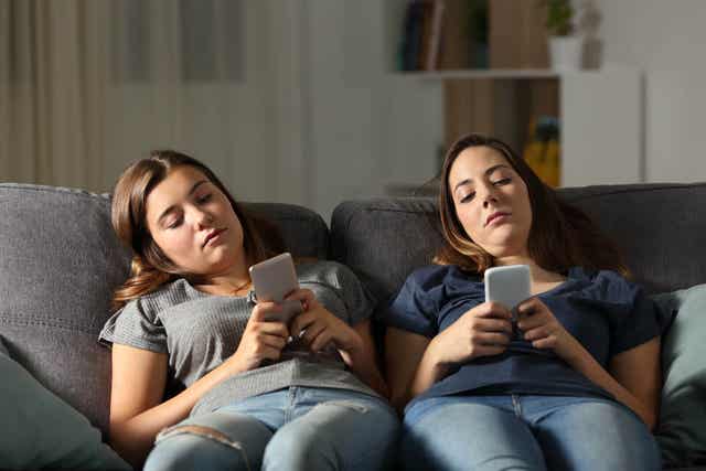 Två ungdomar sitter i soffan med mobilen i handen.